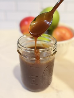 Homemade caramel sauce drizzled from a spoon with fresh apples in the background