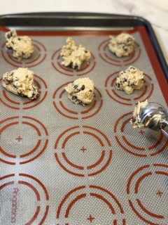 Homemade chocolate chip cookie dough being scooped onto a baking sheet with a cookie scoop.