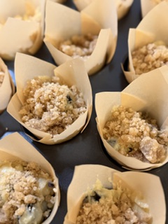 Homemade blueberry muffin batter filled into cupcake liners and topped with a buttery crumble topping, ready to bake.