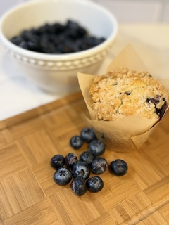 Homemade blueberry muffin on a cutting board with fresh blueberries in a bowl and scattered beside.
