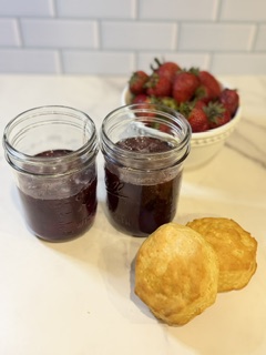 Homemade strawberry jam in glass jars serviced with fresh strawberries and golden homemade biscuits.